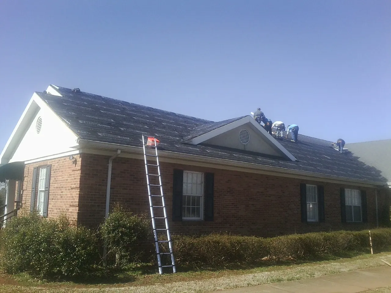 Crew tearing shingles off a brick ranch roof with a ladder set — Emergency Roof Repair work by our crew in Leitchfield