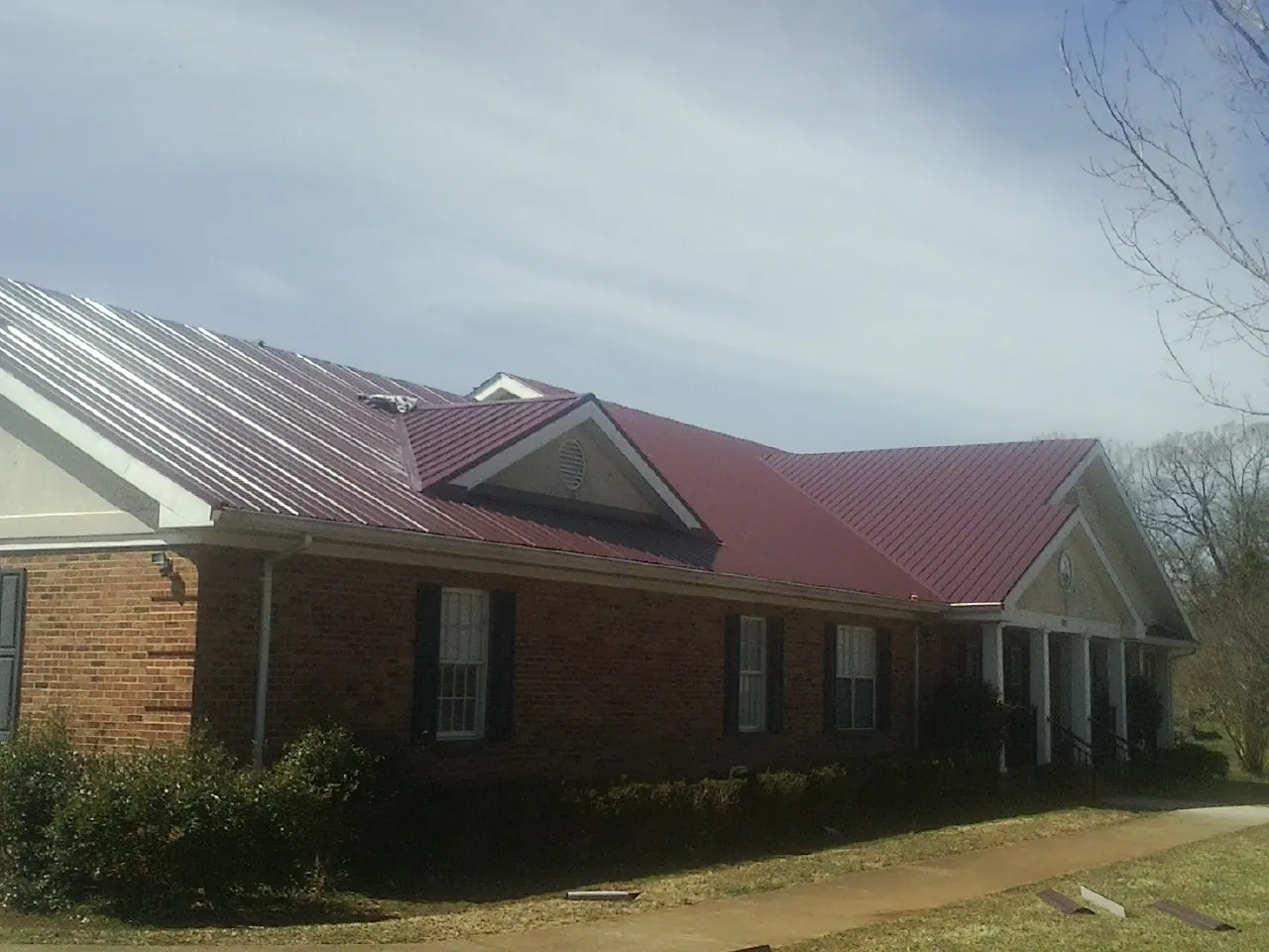Red metal roof with gabled entries on a long brick building, from a Hail Damage Roof Repair job in Leitchfield