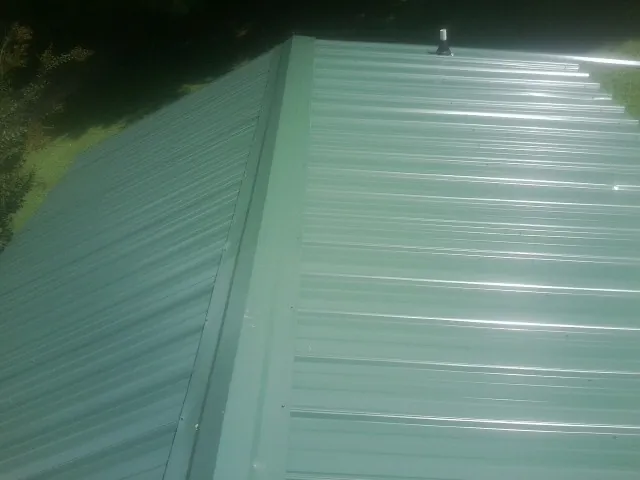 New green metal panels meeting at the ridge of a roof — Flat Roof Repair work by our crew in Leitchfield