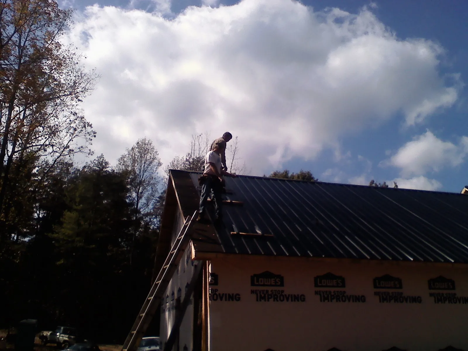 Roofer fastening dark metal panels high against a cloudy sky, from a Roof Inspection job in Leitchfield