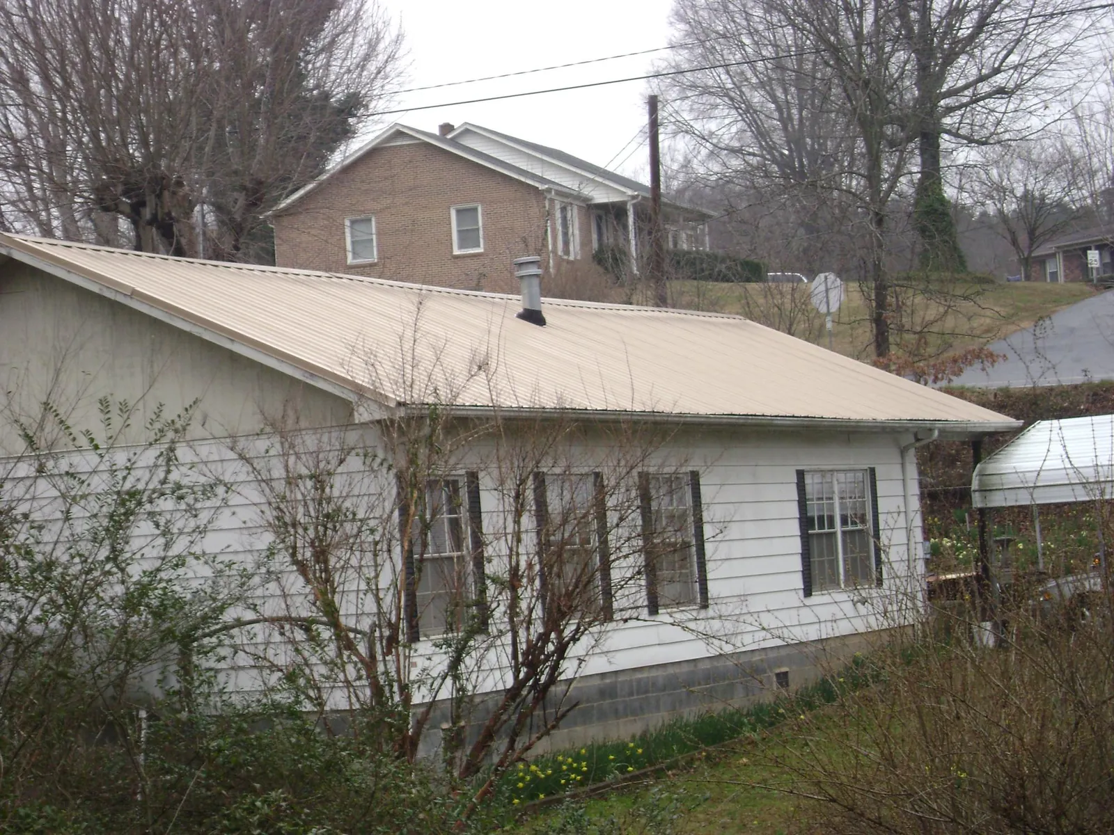 Tan metal roof on a white sided house set into a hillside — Commercial Roofing by Roofing Brothers in Leitchfield