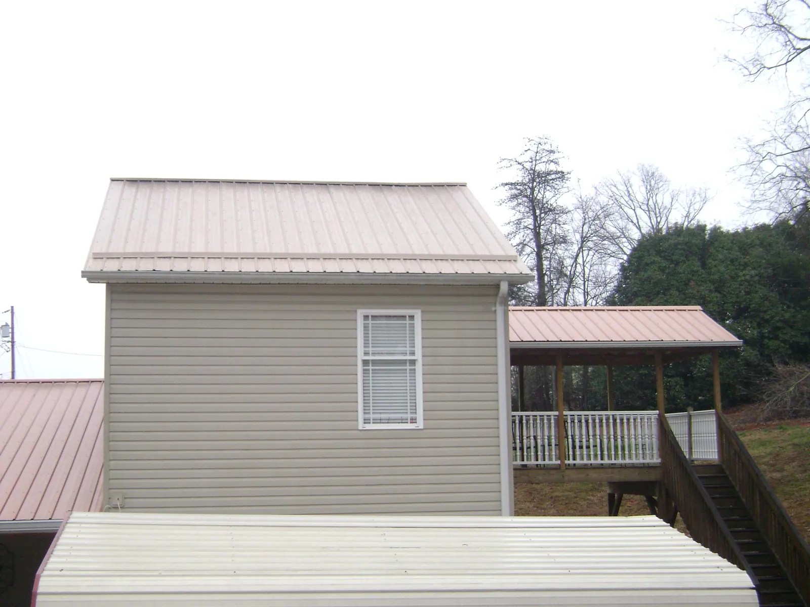 Tan metal roofs on a two story addition and attached porch, from a Roof Replacement job in Leitchfield
